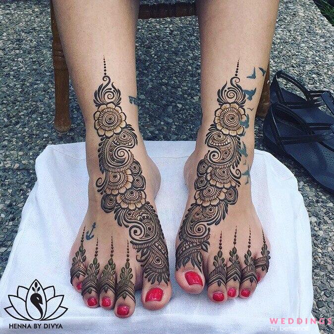 Feet featuring elaborate henna art and painted toenails, poised on white.