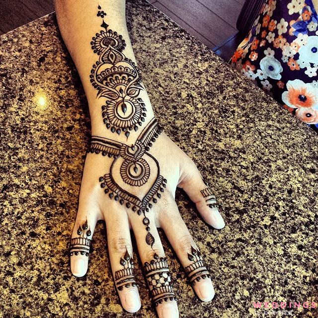 Photo of minimalist mehendi design for back hand, surrounded by flowers on a marble countertop.