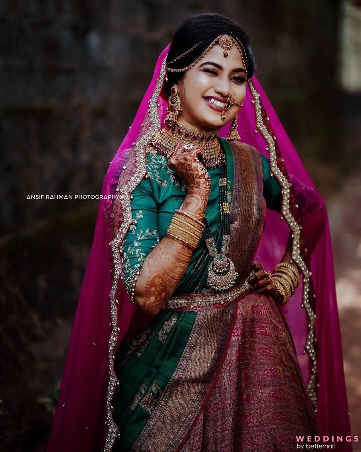 A beautiful Indian woman in a pink sari poses with elegance on a stone wall.