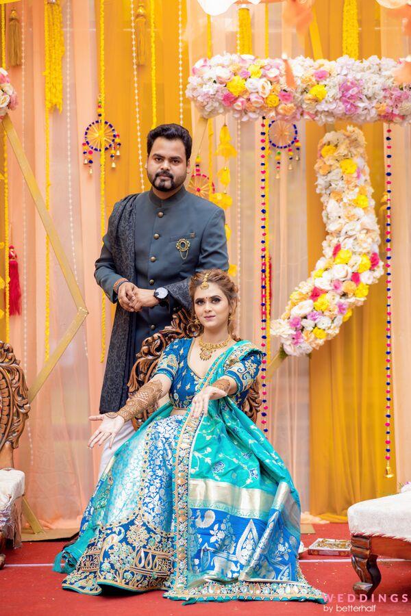 A couple poses in front of a colorful backdrop, showcasing their traditional Indian attire and vibrant accessories.