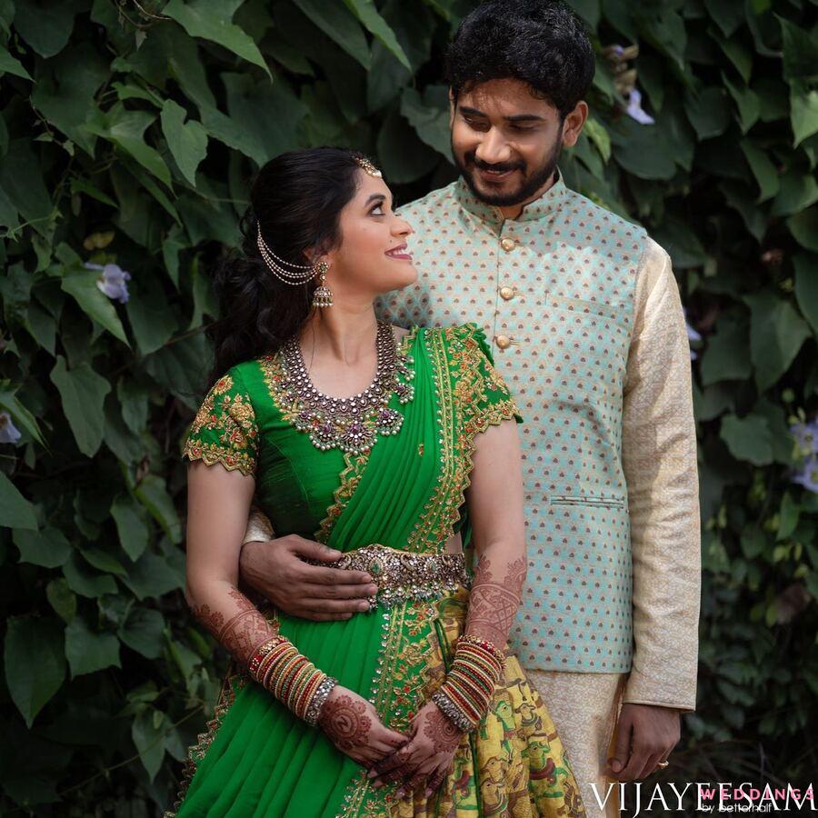 A couple in traditional Indian attire posing in front of a lush green wall surrounded by plants.