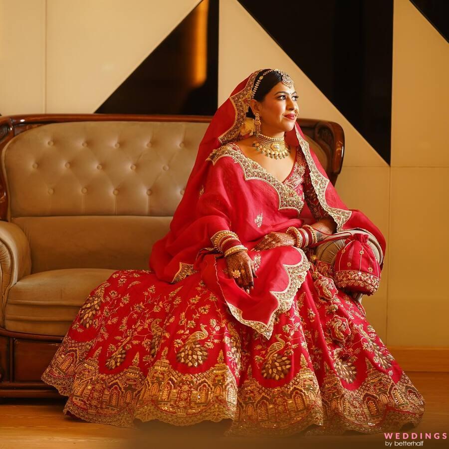 Indian woman in a red lehenga sitting on a stylish chair. Perfect for traditional bridal inspiration.