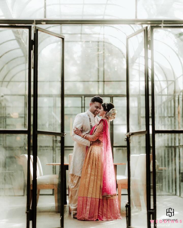 A romantic image of an Indian couple embracing in a glass enclosure at a wedding or engagement session.