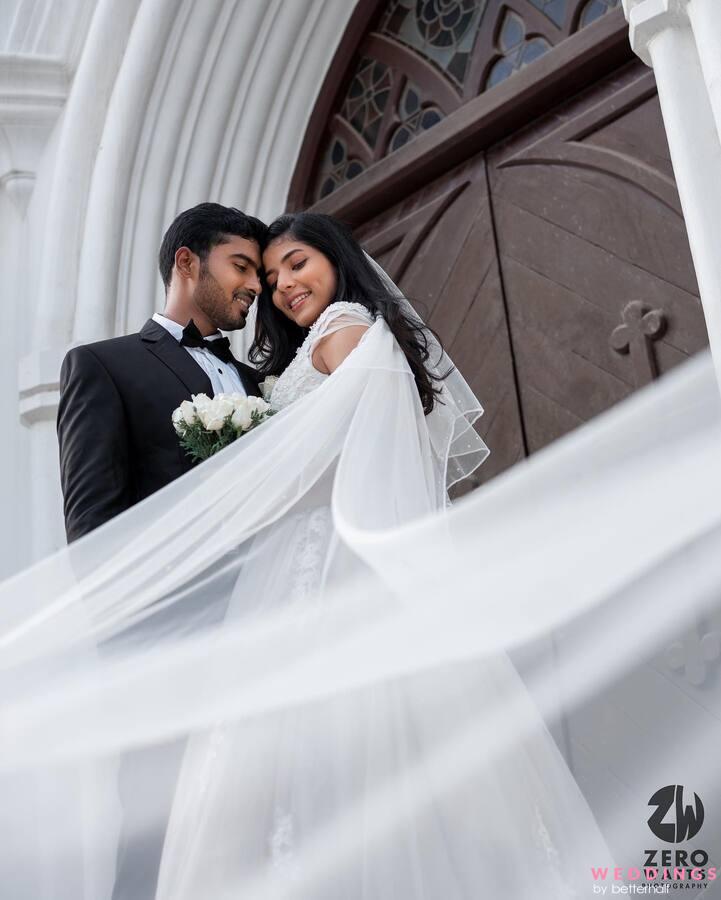 Newlywed couple in a white wedding gown and dark suit pose in front of a church